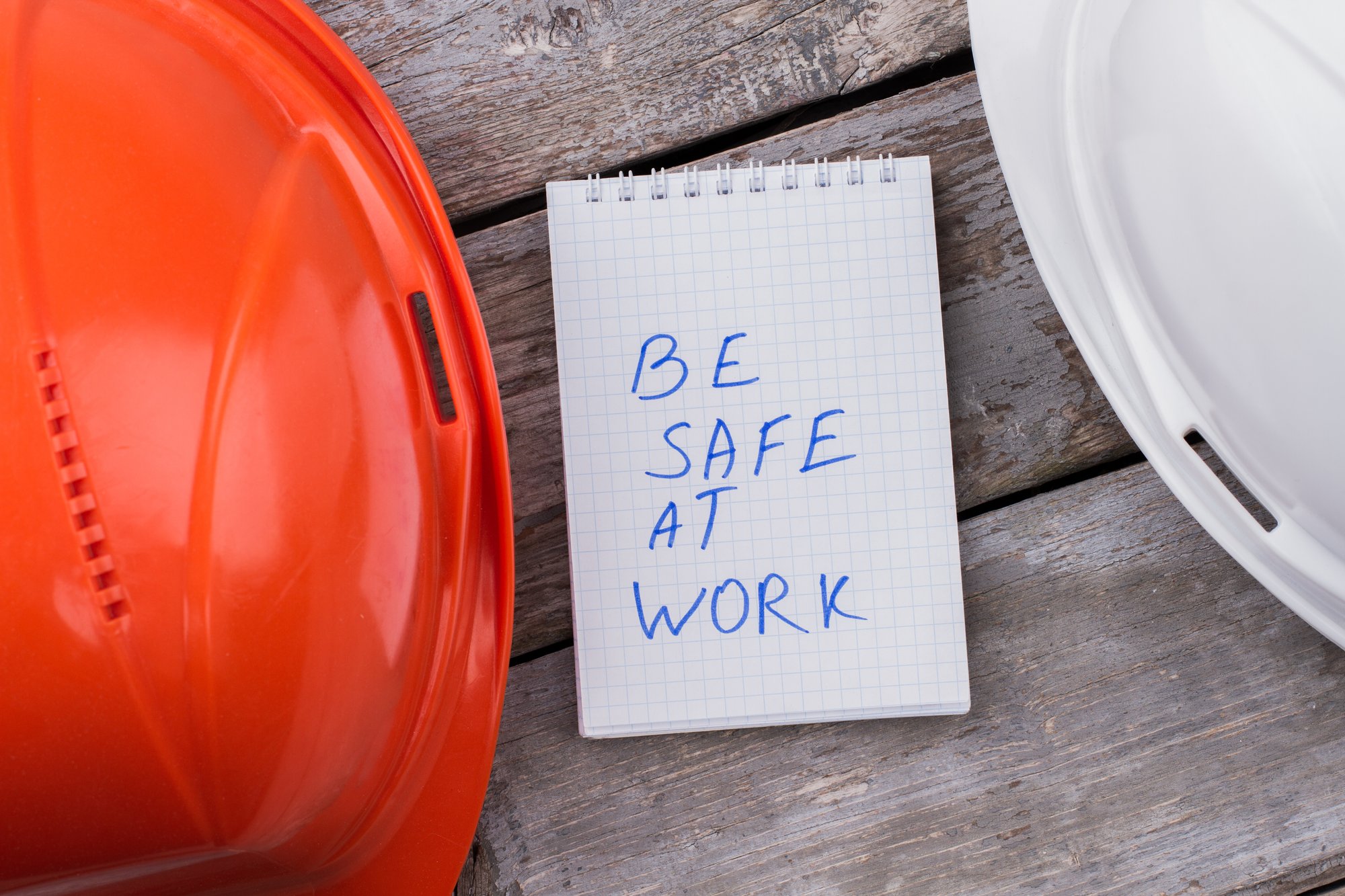 be-safe-work-concept-white-orange-constructor-helmets-notepad-with-be-safe-work-notice-wooden-table